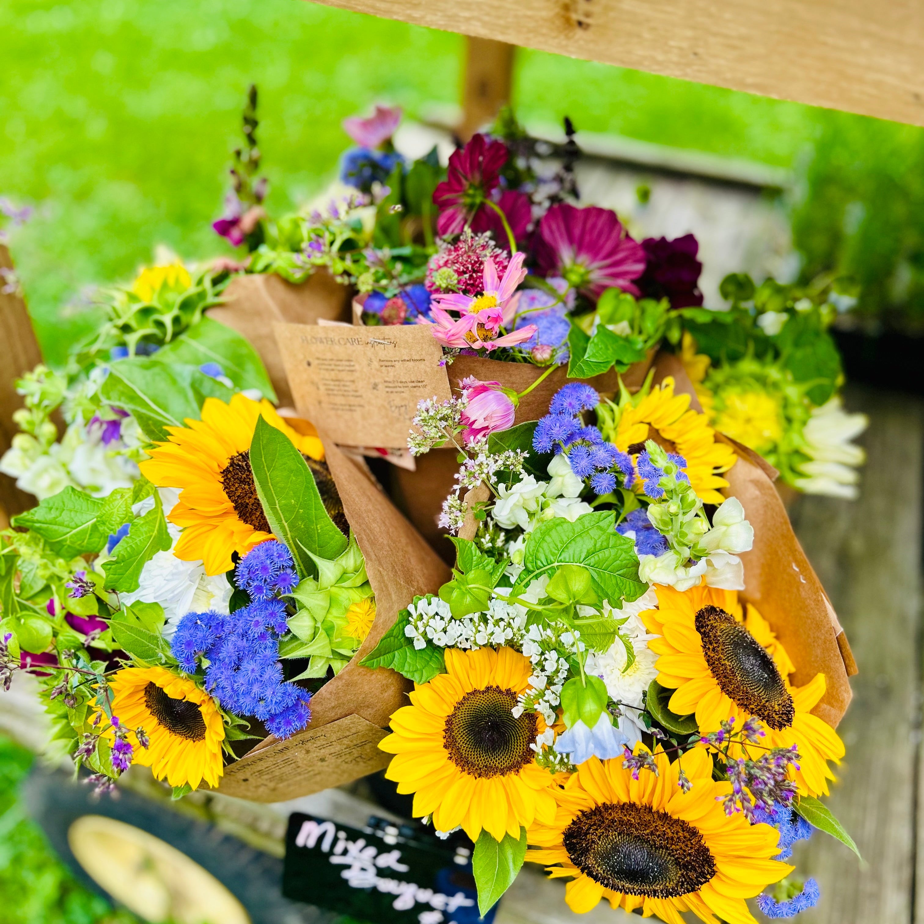 Bouquet of flowers with sunflowers and other varieties in a wooden basket on a grassy background.