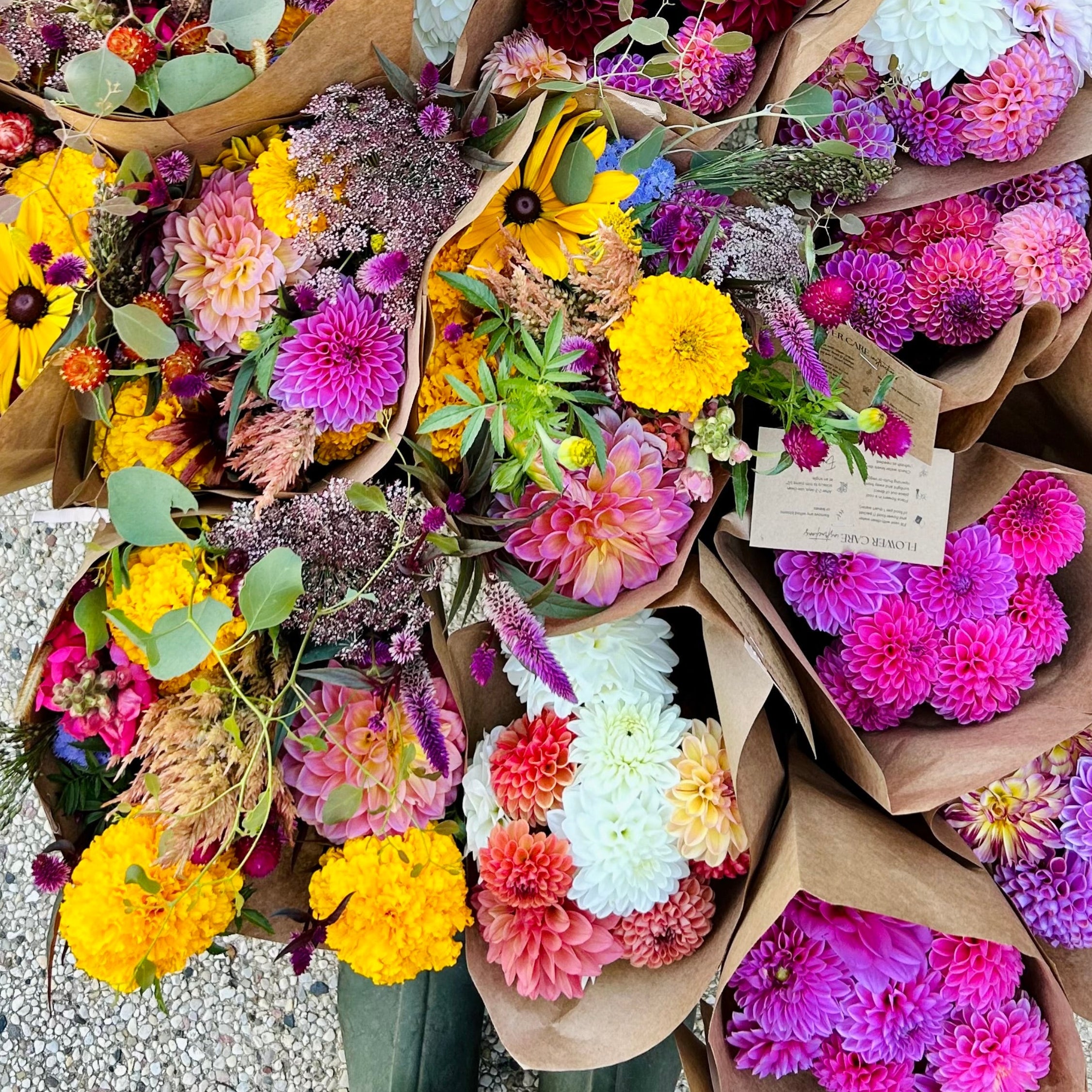 Bouquets of colorful flowers in brown paper packaging on a stone surface.